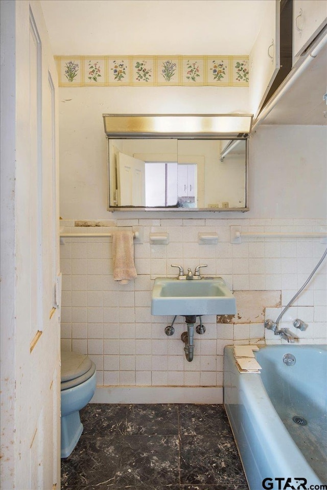 bathroom with a washtub, sink, tile walls, and toilet