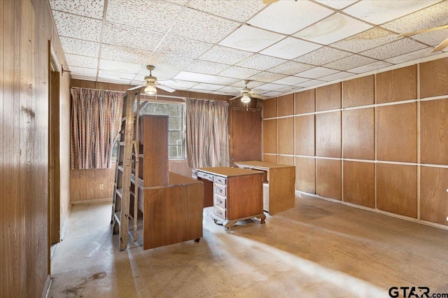 unfurnished office featuring ceiling fan, a paneled ceiling, and wooden walls