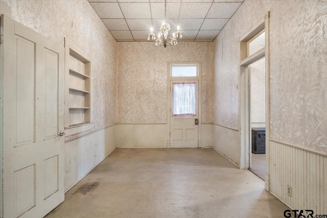 empty room featuring built in shelves, a paneled ceiling, and a chandelier