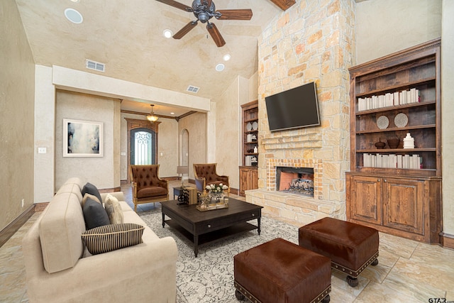 living room with built in shelves, high vaulted ceiling, a stone fireplace, and ceiling fan