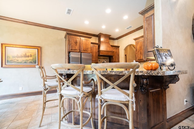 kitchen with premium range hood, crown molding, kitchen peninsula, a breakfast bar area, and stainless steel refrigerator