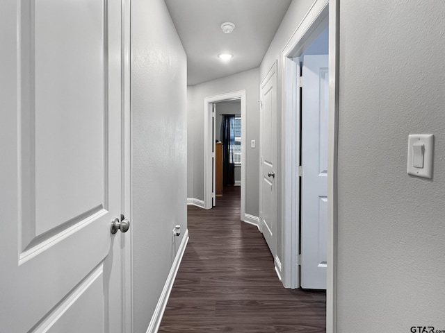 corridor featuring dark wood-style floors, a textured wall, and baseboards