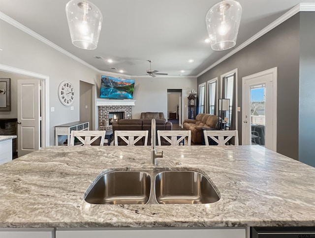 kitchen featuring ornamental molding, a fireplace, a sink, and light stone countertops