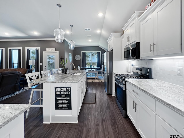 kitchen featuring a breakfast bar, appliances with stainless steel finishes, white cabinetry, a center island with sink, and decorative light fixtures