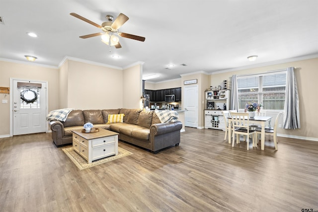 living area with a wealth of natural light, crown molding, light wood-style flooring, and baseboards