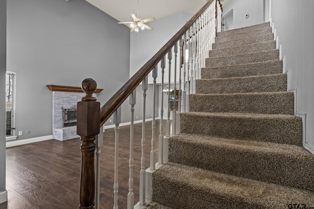 staircase with a brick fireplace, baseboards, a high ceiling, and wood finished floors