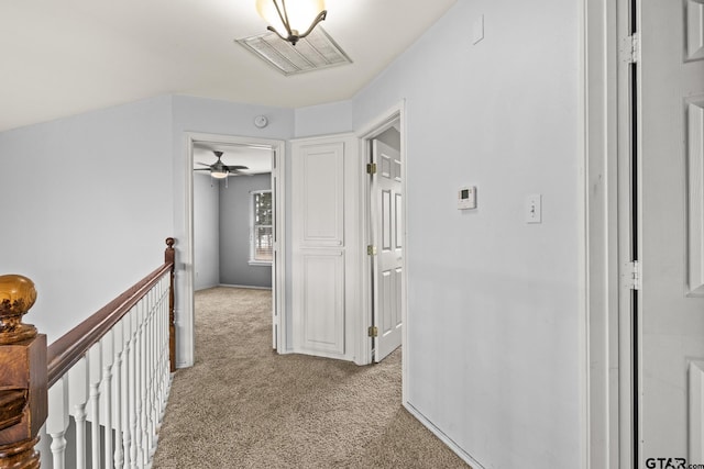 hall with light carpet, visible vents, and an upstairs landing