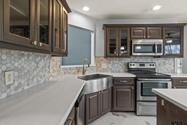 kitchen featuring glass insert cabinets, appliances with stainless steel finishes, marble finish floor, light countertops, and a sink