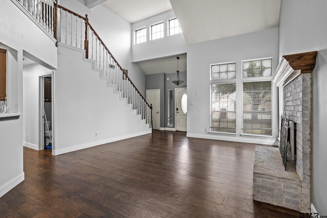 unfurnished living room featuring a fireplace, dark wood finished floors, stairway, and baseboards