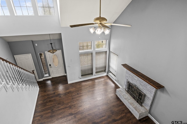 living room with dark wood-type flooring, a ceiling fan, a brick fireplace, high vaulted ceiling, and baseboards