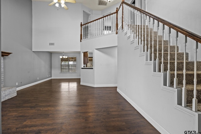 unfurnished living room with visible vents, baseboards, dark wood finished floors, stairway, and ceiling fan with notable chandelier