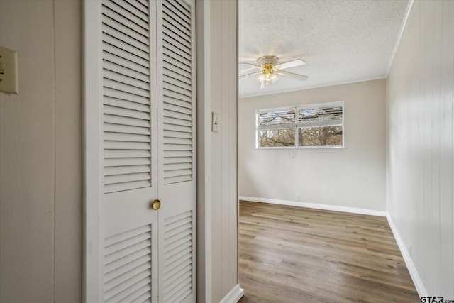 unfurnished bedroom with crown molding, ceiling fan, wooden walls, light hardwood / wood-style floors, and a textured ceiling