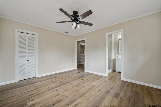 unfurnished bedroom featuring ensuite bathroom, light hardwood / wood-style flooring, ceiling fan, crown molding, and a closet