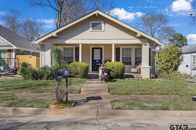 bungalow with covered porch, fence, a front lawn, and brick siding