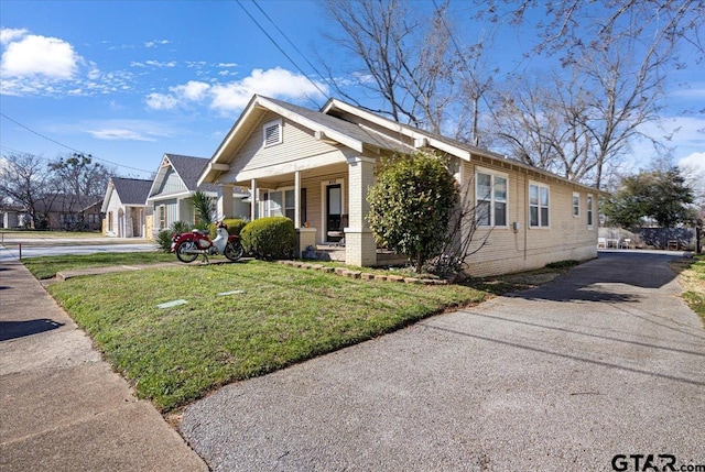 view of front of property with a porch, brick siding, a front lawn, and aphalt driveway