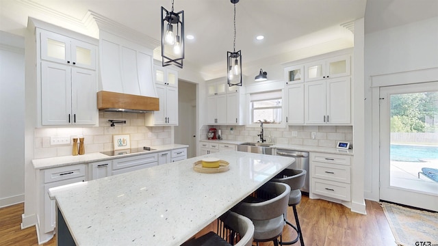 kitchen featuring stainless steel dishwasher, a center island, black electric cooktop, white cabinetry, and a sink