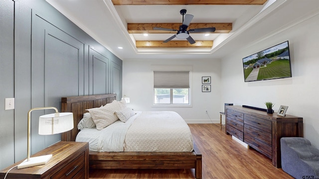 bedroom with beam ceiling, a ceiling fan, baseboards, light wood-type flooring, and a tray ceiling