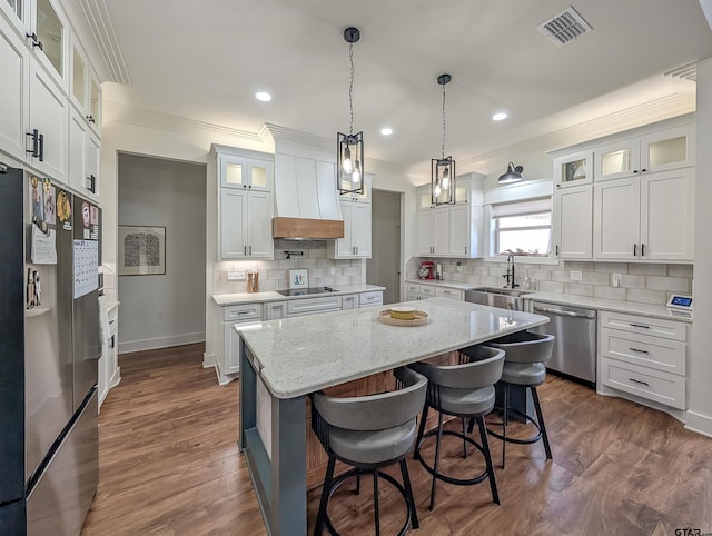 kitchen with a sink, ornamental molding, stainless steel appliances, a kitchen island, and custom exhaust hood