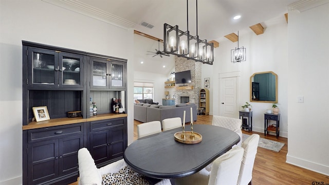 dining room featuring a fireplace, baseboards, high vaulted ceiling, ceiling fan with notable chandelier, and light wood finished floors