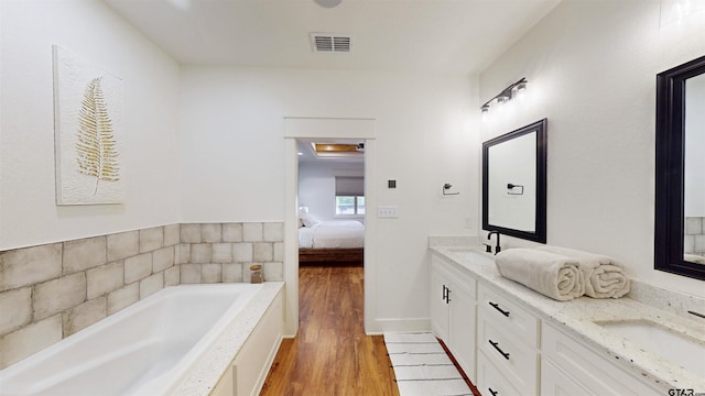 ensuite bathroom with visible vents, double vanity, wood finished floors, ensuite bathroom, and a sink
