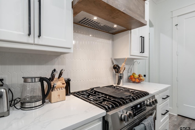 kitchen featuring custom range hood, light stone countertops, stainless steel gas range, and white cabinetry