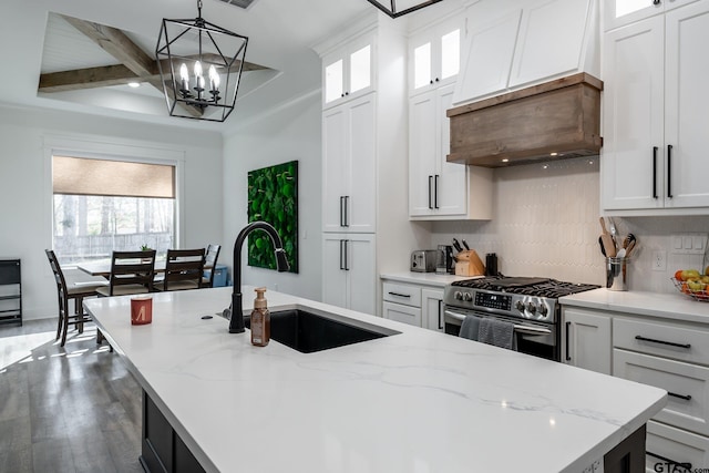 kitchen featuring a center island with sink, hanging light fixtures, sink, stainless steel range, and white cabinets