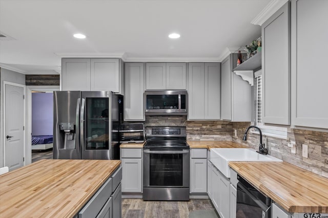 kitchen with stainless steel appliances, sink, wooden counters, backsplash, and gray cabinetry