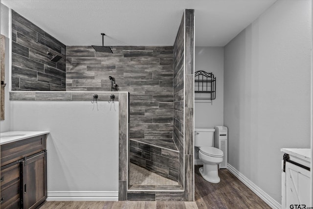 bathroom with hardwood / wood-style flooring, vanity, toilet, and a tile shower