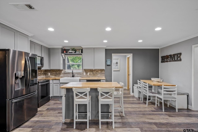 kitchen featuring stainless steel appliances, gray cabinets, a kitchen island, a breakfast bar, and wood counters