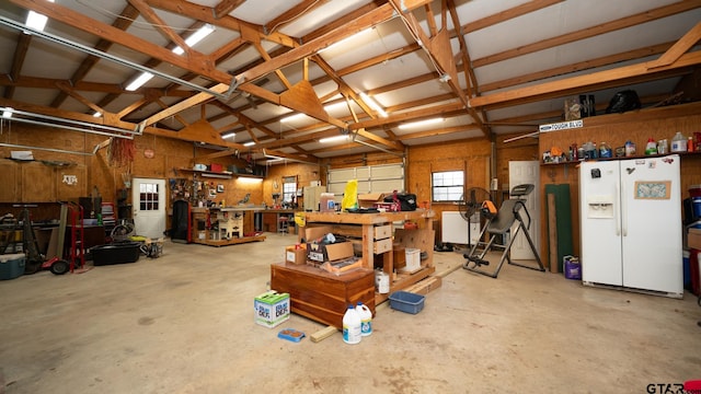 garage featuring white refrigerator with ice dispenser and a workshop area