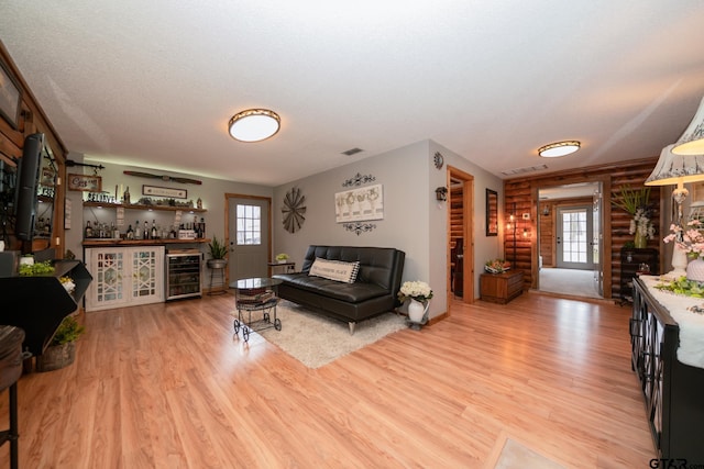 living room featuring wine cooler, light hardwood / wood-style floors, a textured ceiling, log walls, and indoor bar