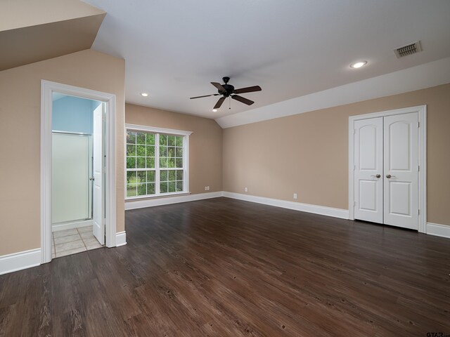 empty room with dark wood-style flooring, visible vents, baseboards, a ceiling fan, and vaulted ceiling