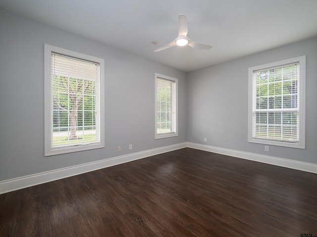 empty room featuring dark wood finished floors, baseboards, ceiling fan, and a wealth of natural light