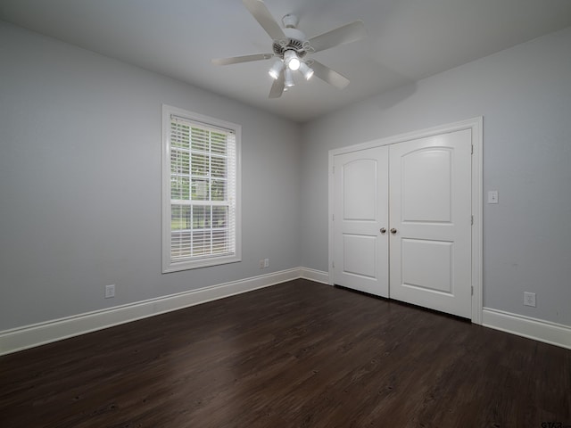 unfurnished bedroom featuring dark wood-style flooring, a closet, baseboards, and ceiling fan
