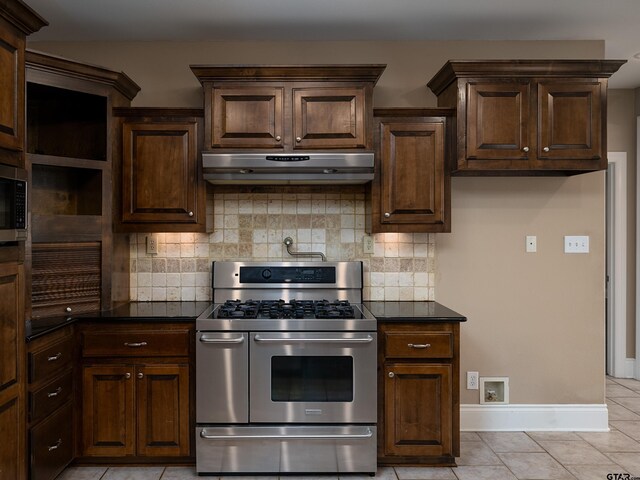 kitchen featuring appliances with stainless steel finishes, exhaust hood, light tile patterned floors, dark countertops, and decorative backsplash