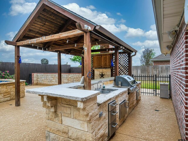 view of patio featuring exterior kitchen, a fenced backyard, a gazebo, a grill, and a sink