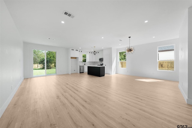 unfurnished living room with plenty of natural light, a notable chandelier, and light hardwood / wood-style flooring