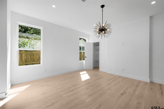 empty room featuring an inviting chandelier and light hardwood / wood-style flooring