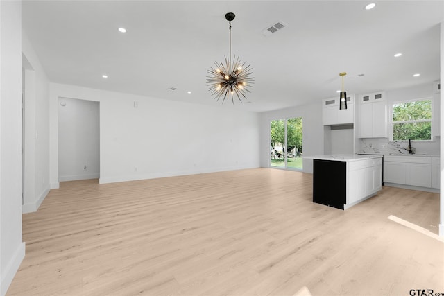 unfurnished living room with an inviting chandelier, a healthy amount of sunlight, and light hardwood / wood-style flooring