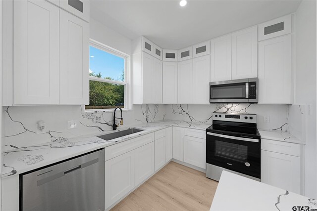 kitchen featuring white cabinetry, appliances with stainless steel finishes, light stone countertops, sink, and light hardwood / wood-style floors