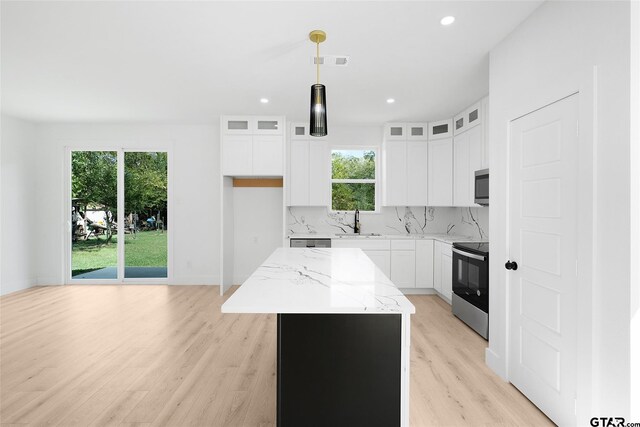 kitchen featuring white cabinetry, stainless steel appliances, light stone countertops, and a center island