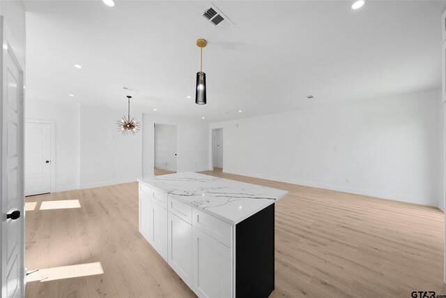 kitchen featuring white cabinetry, light hardwood / wood-style flooring, pendant lighting, light stone countertops, and a center island