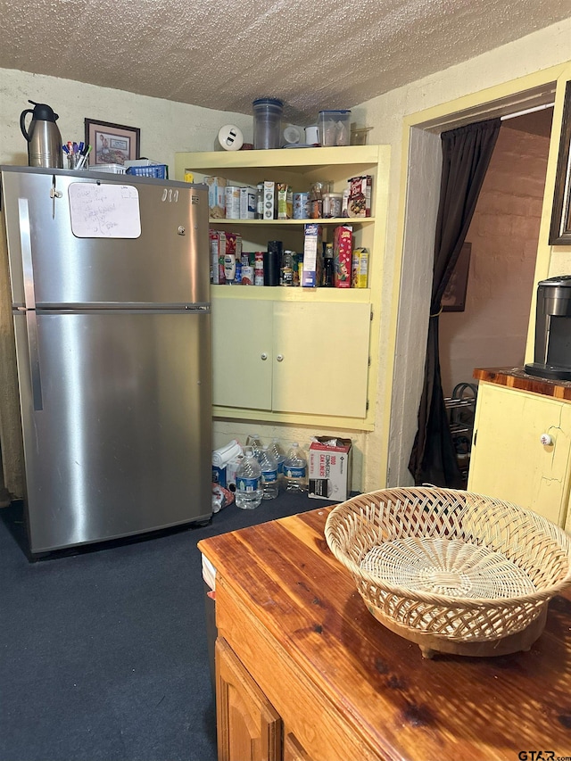 interior space featuring a textured ceiling, stainless steel refrigerator, and wood counters