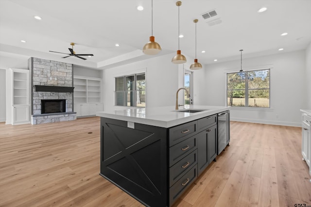 kitchen with built in shelves, a kitchen island with sink, ceiling fan, sink, and decorative light fixtures