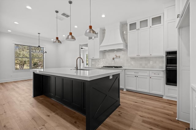 kitchen with white cabinetry, tasteful backsplash, pendant lighting, a center island with sink, and custom exhaust hood