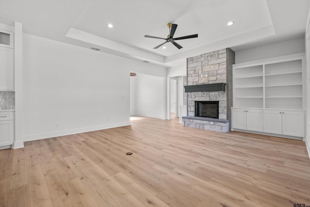 unfurnished living room with a raised ceiling, light hardwood / wood-style flooring, a stone fireplace, and ceiling fan