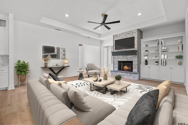 living room with a tray ceiling, ceiling fan, a fireplace, and light hardwood / wood-style floors