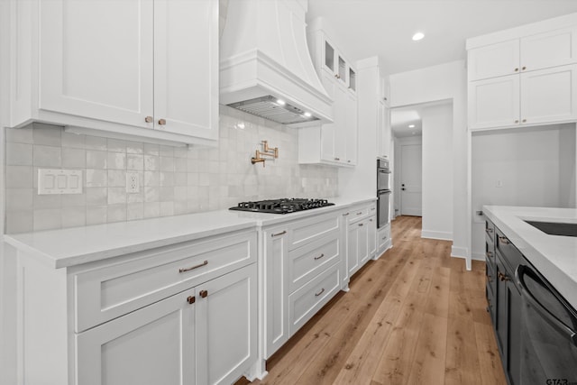 kitchen featuring custom exhaust hood, white cabinets, decorative backsplash, light wood-type flooring, and gas cooktop