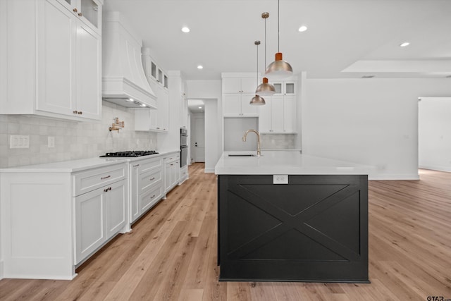 kitchen featuring pendant lighting, white cabinets, sink, an island with sink, and light hardwood / wood-style floors