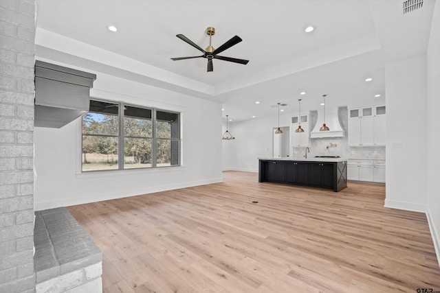 unfurnished living room with a tray ceiling, ceiling fan, light hardwood / wood-style flooring, and sink